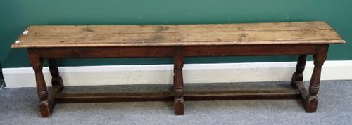 A 17th century style oak bench, the single plank rectangular top on six turned supports, 182cm wide x 48cm high x 29cm deep.