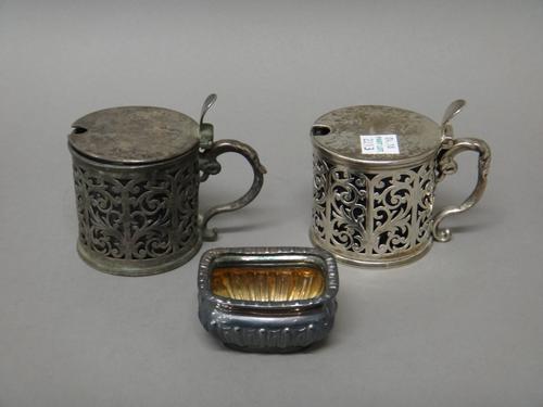 A pair of Victorian silver mustard pots, each with scroll pierced decoration, with an oval thumbpiece and with a hollow scrolling handle, with differi