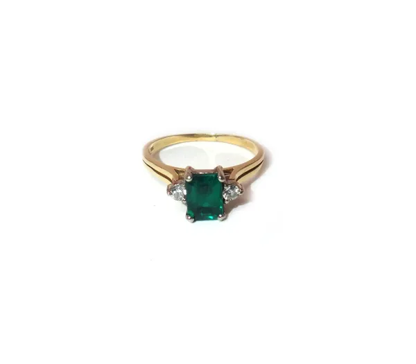 A gold, synthetic emerald and diamond three stone ring, claw set with the cut cornered rectangular step cut emerald between two circular cut diamonds,