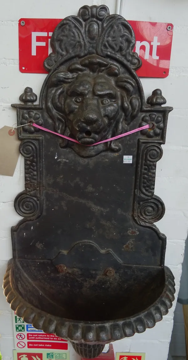 A cast iron wall font, 20th century, with relief cast iron lion's head spout over a fluted demi-lune basin. 80cm high.