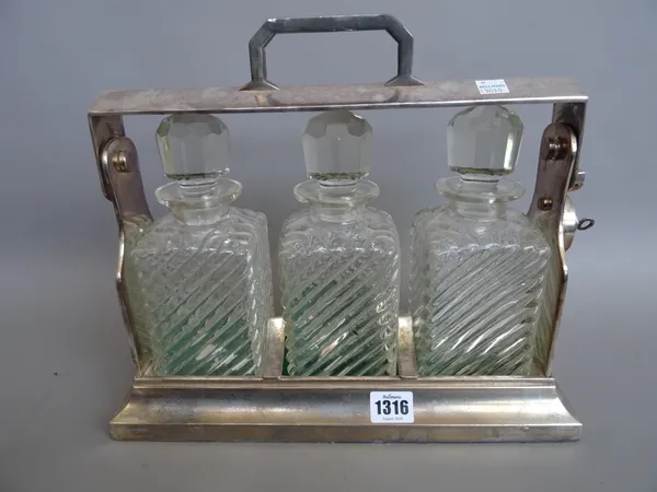 A silverplated three bottle cased tantalus, early 20th century, with locking mechanism, on a plinth base, enclosing three glass decanters and stoppers