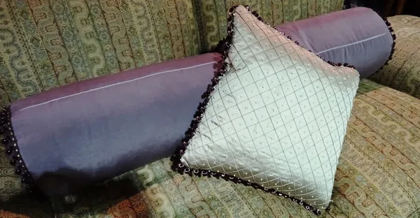 Cushions, a pair of purple silk bolster cushions with purple glass beads, together with a silver silk cushion with matching glass beads (3).  H5