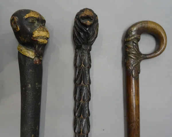 An ebonised 'lion's head' carved wooden walking stick, 19th century, with foliate carved shaft (87cm), a polychrome painted 'monkey head' walking stic