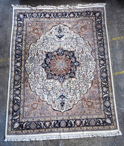 An Indian carpet, the ivory field with a bold dark indigo lobed medallion, beige spandrels, all with floral sprays; a dark indigo palmette, leaf and v