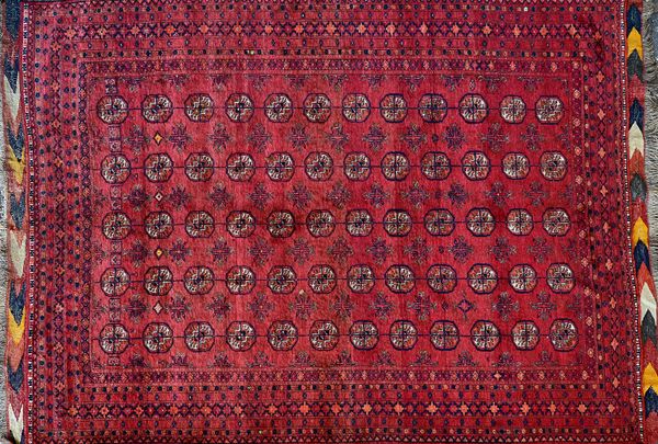 An Afghan Turkman carpet, the madder field with five columns of twelve guls, supported by crosses, 250 x 189cm.