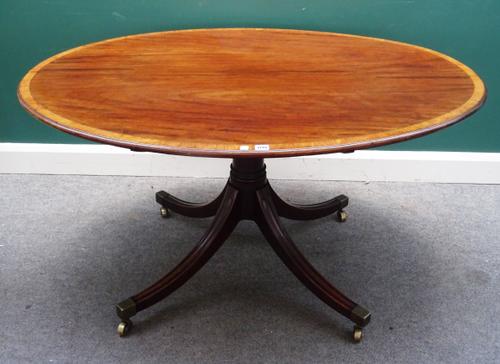 A George III crossbanded mahogany oval snap top centre table, on four downswept supports, 137cm wide x 72cm high x 102cm deep.