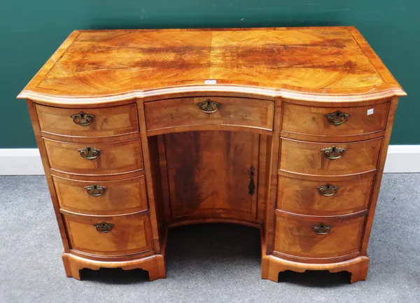 A George I style feather banded walnut double bowfront knee hole writing desk, with nine drawers about the centre cupboard on bracket feet, 111cm wide