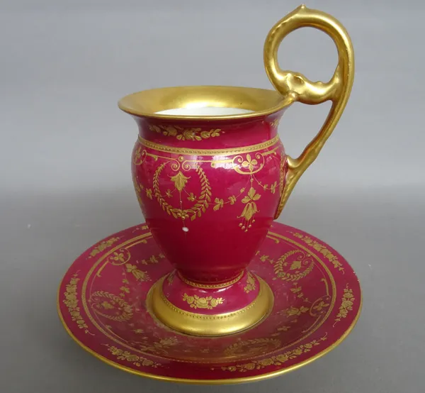 A Berlin porcelain claret-ground cabinet cup and saucer, circa 1915-18, the cup set with high gilt acanthus moulded handle, each piece gilt with flora