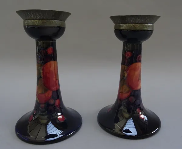 A pair of Moorcroft pottery candlesticks, decorated in the 'Pomegranate' pattern, circa 1920, each with Tudric pewter mounts to the sconce, painted an