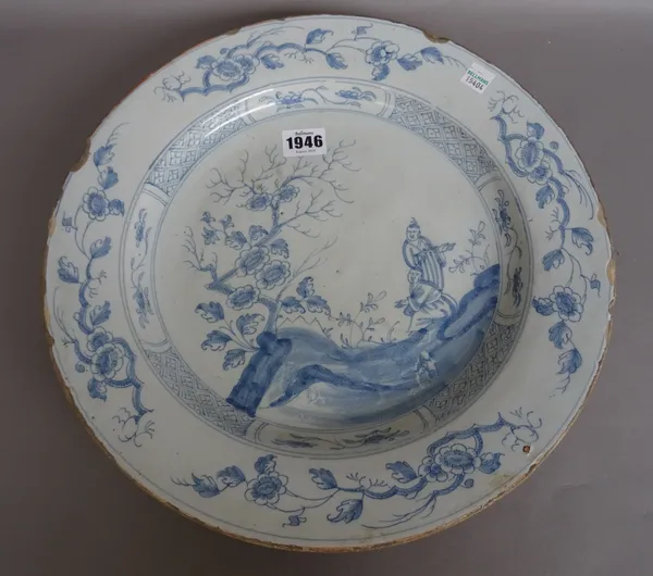 An English delftware blue and white large plate, perhaps Bristol,circa 1760, painted with two Oriental figures  beside a flowering tree, the border pa