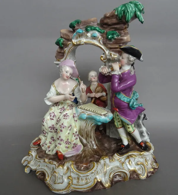 A late 19th century Meissen porcelain musical group, outside decorated, depicting three figures under an arbour on a gilt C -scroll base, blue crossed