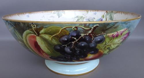 A Limoges porcelain footed bowl, 20th century, of large proportions, hand painted with fruit against a riverscape, red printed mark. 44.5cm diameter.