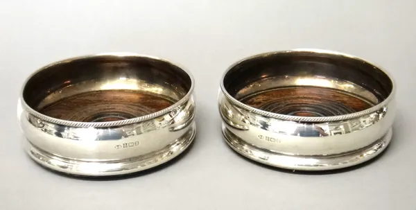 A pair of silver mounted circular bottle coasters, decorated with gadrooned rims and having turned wooden bases, Birmingham 1976, (pair).