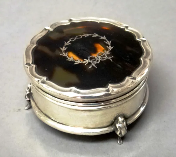 A silver and tortoiseshell lidded shaped circular trinket box, the hinged lid inlaid with a wreath motif, the base raised on three feet, Birmingham 19