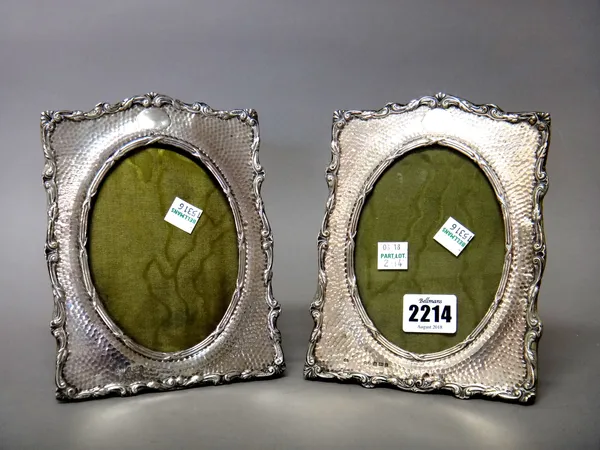 A pair of silver mounted shaped rectangular photograph frames, each with a central oval aperture, the mount with martele decoration, within a foliate