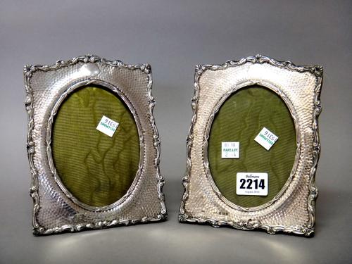A pair of silver mounted shaped rectangular photograph frames, each with a central oval aperture, the mount with martele decoration, within a foliate