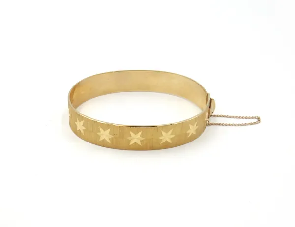 A 9ct gold oval hinged bangle, decorated with a row of bright cut stars, fitted with a safety chain, London 1970, weight 20 gms.