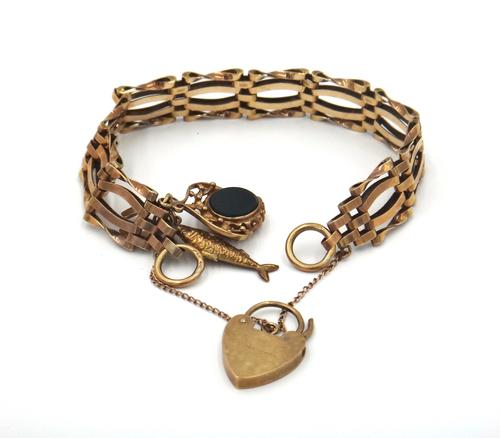 A 9ct gold curved bar, twisted bar and oval link gate bracelet, fitted with three pendants and charms, comprising; a fish, a horseshoe and a rotating