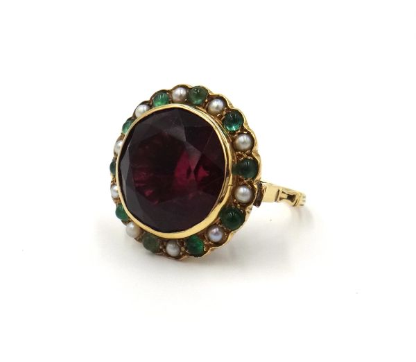 A gold ring, collet set with a circular cut magenta coloured tourmaline to the centre, in a surround of alternating cabochon emeralds and cultured pea