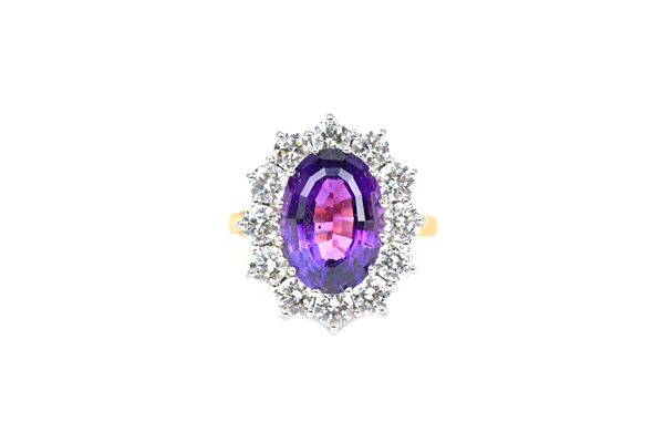 An 18ct gold, amethyst and diamond oval cluster ring, claw set with the oval cut amethyst in a surround of twelve circular cut diamonds, ring size app