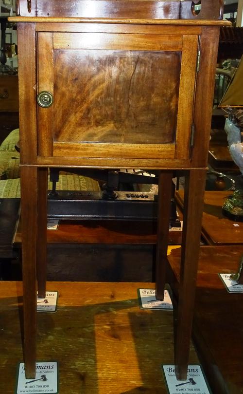 An early 19th century mahogany bedside cupboard with a three quarter wooden gallery and a slatted base below a single panelled door and tapering legs,