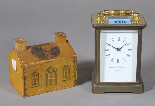 Matthew Norman; a 20th century brass carriage clock, 8cm wide x 11cm high, and a 20th century painted wooden money bank, 10cm wide x 9cm high, (2).