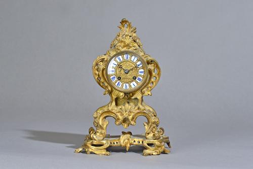 A French rococo style ormolu mantel clock, late 19th century, the foliate scroll case with inset enamel Roman numerals enclosing a two train movement