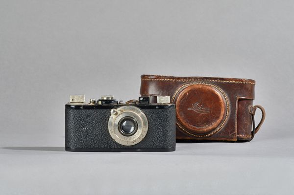 A Leica Elmar camera, circa 1928, ebonised finish, with a Leitz 1:35F 50mm lens and leather carry case. Illustrated.
