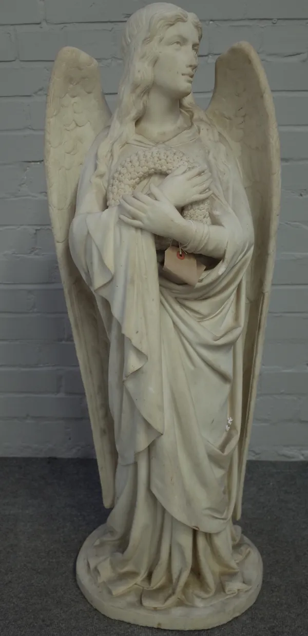 A late 20th century marble angel figure, carved arms folded across a floral wreath, 106cm high.