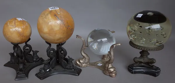 Two yellow marble spheres raised on griffin cast tri-form bases, 25cm high another similar, the larger glass sphere with air bubble inclusions on a me