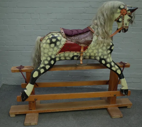 A dapple grey wooden rocking horse, early 20th century, mounted on a pine and wrought iron swing frame base, 122cm high.