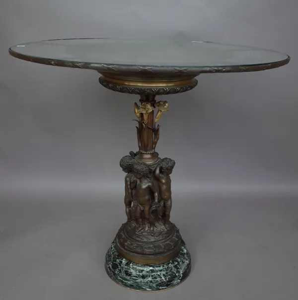 A bronze figural centrepiece table, late 20th century, the circular glass top over a relief cast charger supported over a fluted column by putto figur