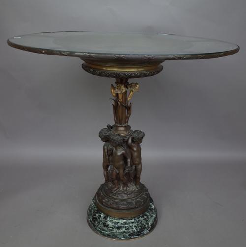 A bronze figural centrepiece table, late 20th century, the circular glass top over a relief cast charger supported over a fluted column by putto figur