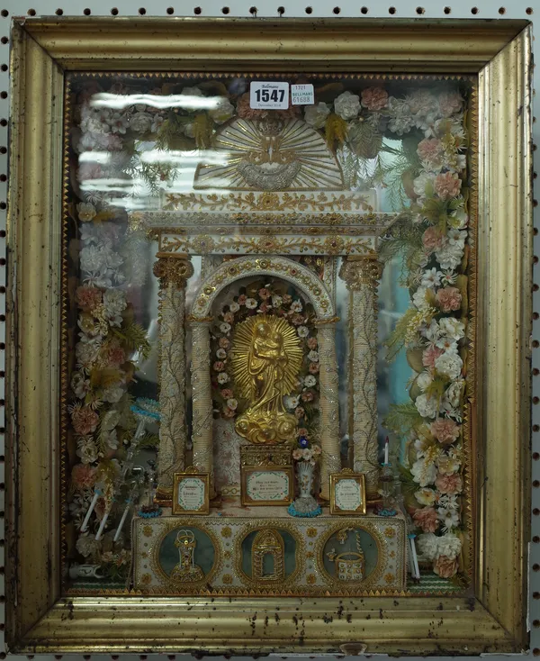 An early 20th century wall mounted shrine, depicting a gilt metal Jesus under a silk and beadwork arch over an altar decorated with miniature glass ca