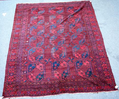 An Afghan Esari carpet, the dark madder field with three columns of six bold guls, single supporting flowerheads, a diamond border, 360cm x 300cm.
