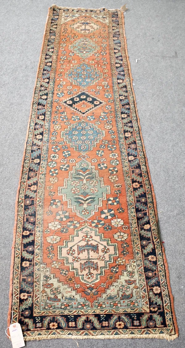 A North West Persian runner, the madder field with seven medallions flowerhead sprays, an indigo leaf and flower border, 326cm x 82cm.