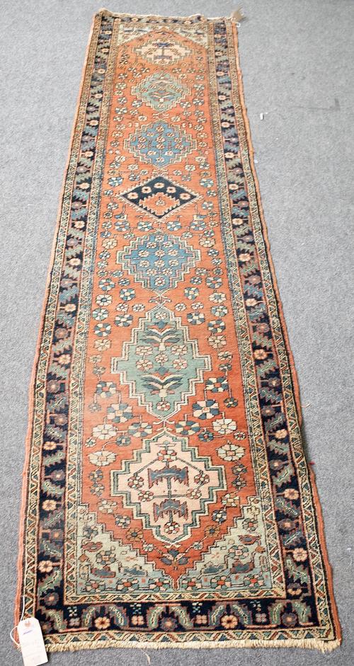 A North West Persian runner, the madder field with seven medallions flowerhead sprays, an indigo leaf and flower border, 326cm x 82cm.