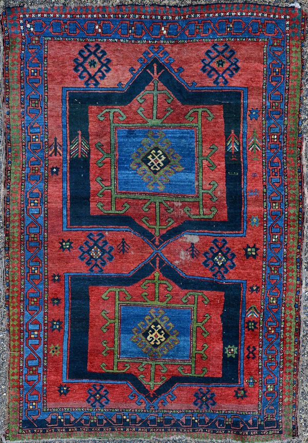 A Kazakh rug, Caucasian, the madder field with two bold medallions, each bearing a stepped diamond, supporting hooked motifs and flowers, an indigo wa