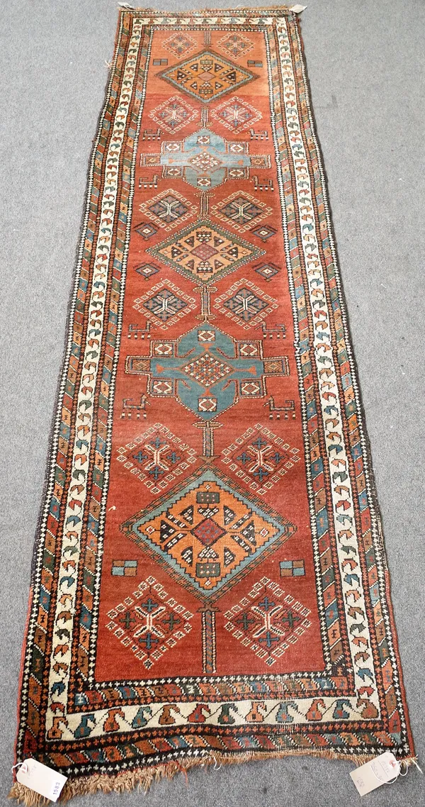 A North West Persian runner, the madder field with five bold medallions, pairs of diamonds, goats, three minor borders, 350cm x 95cm.