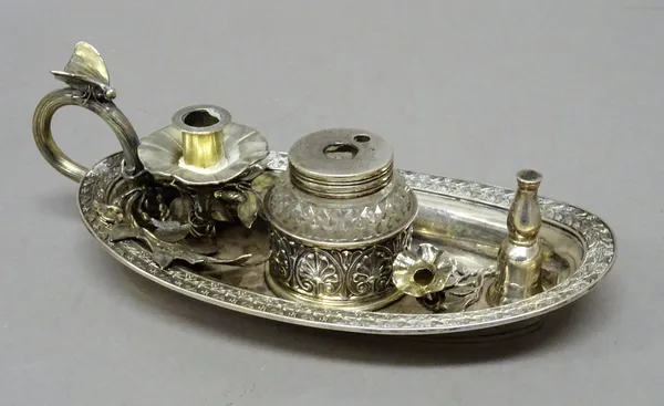 A George IV silver inkstand, of oval form, decorated with a foliate border, fitted with a silver mounted single faceted glass ink bottle, a candle hol