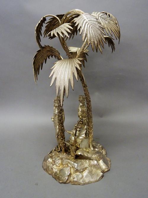 A Victorian silver table centrepiece, modelled as two palm trees raised on a rocky base, mounted with the standing figures of two gentlemen, one weari