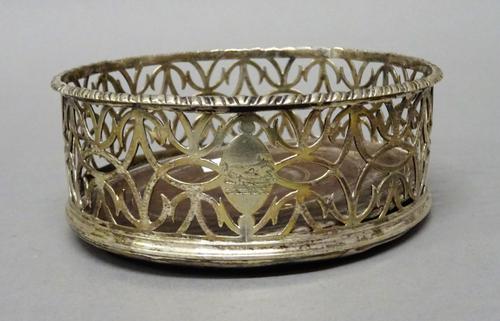 A George III silver bottle coaster, of pierced circular form, with a cast gadrooned rim and with a turned wooden base, diameter 12cm, London probably