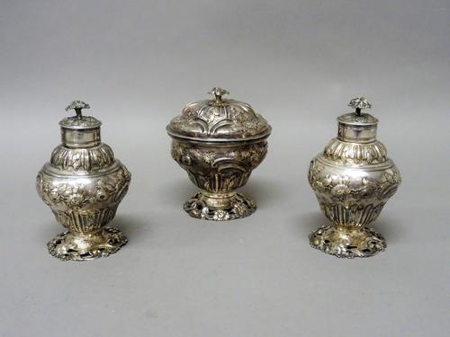 A late George II silver sugar box and cover and a matching pair of late George II silver tea caddies, each of baluster form with floral, foliate and s