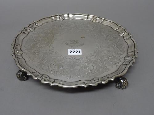 A George II silver salver, of shaped circular form, having a pie-crust rim, raised on four scrolled feet, crest and motto engraved to the centre, othe