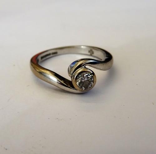 An 18ct white gold and diamond single stone ring, gypsy set with a circular cut diamond in a crossover design, ring size K and a half, with a case.