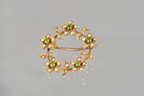 A gold, demantoid garnet and seed pearl set brooch, in a circular design, with five flowerheads, each centred by a demantoid garnet, with a case. Illu