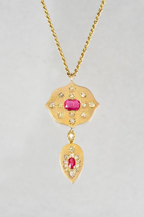 A gold, ruby and diamond set pendant, with a shaped oval top centered by an oval cut ruby and otherwise set with twelve cushion shaped diamonds, the f