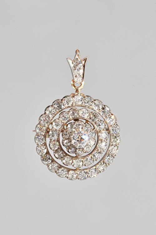 A gold and silver set, diamond pendant brooch, in a stepped circular openwork design, mounted with the principal cushion shaped diamond to the centre,