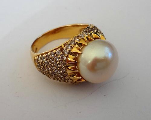 A gold, cultured pearl and colourless gem set ring, mounted with the cultured pearl to the centre, between colourless gem set shoulders, detailed 18 K