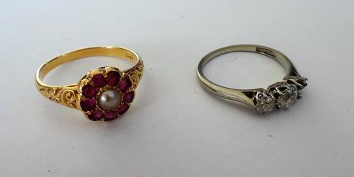 A gold, ruby and half pearl set cluster ring, mounted with the half pearl to the centre, in a surround of nine cushion shaped rubies, between scroll d